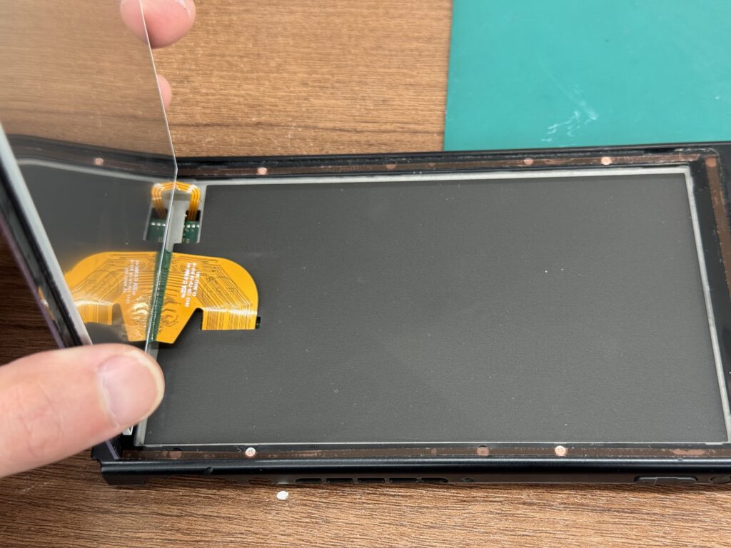 背面カバーを開け、内部の基板やパーツが見えている状態、または破損した液晶を取り外している途中の写真