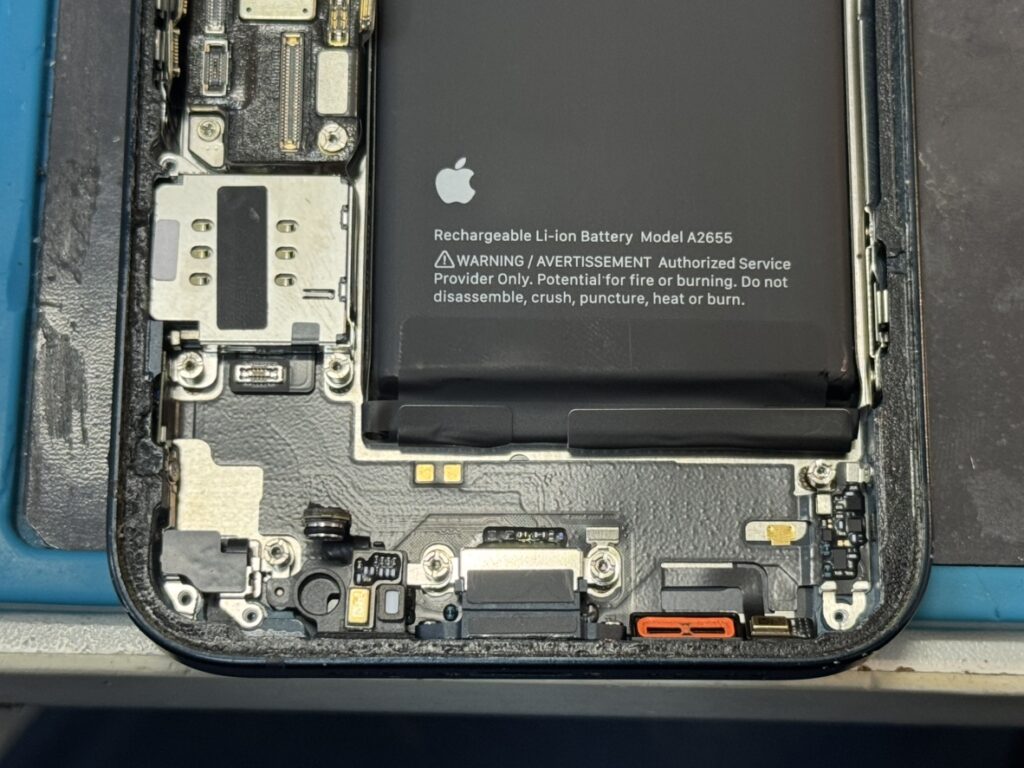 iPhone 13の充電口交換修理中。本体を分解し、故障したドックコネクタを取り外して新しいパーツへ交換する作業風景