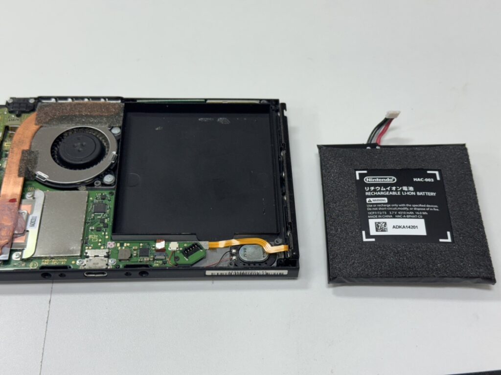 Switchの背面を開き、パンパンに膨らんだ古いバッテリーを安全に取り出している様子。