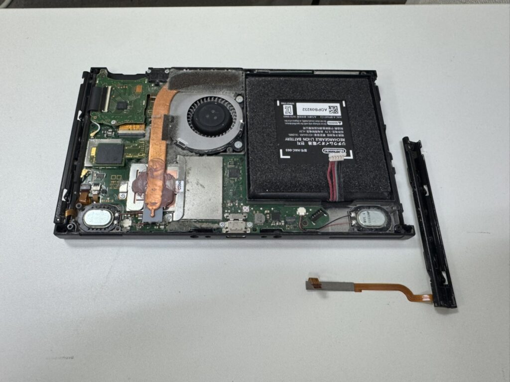 Switchの背面を開き、故障した本体側のスライドレールを取り外している修理作業。