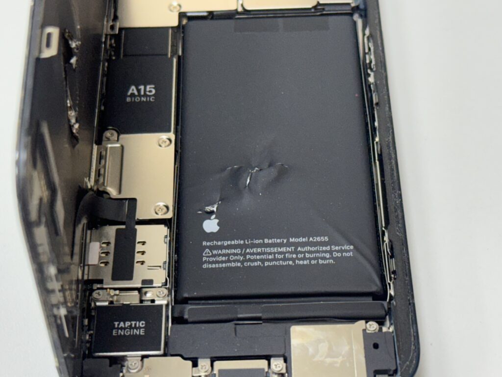 iPhone 13の内部。工具が刺さったバッテリーと画面パネルを取り外している特殊修理の様子。