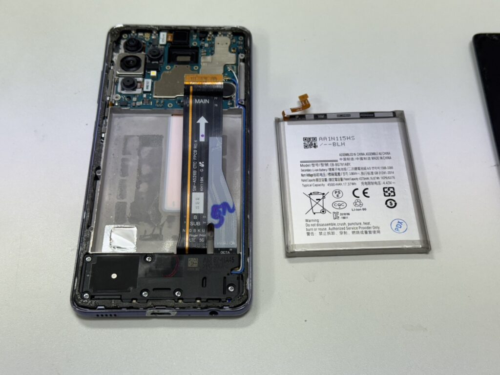 Galaxy A52 5Gの背面を開き、基板から寿命を迎えた古いバッテリーを取り外している様子。