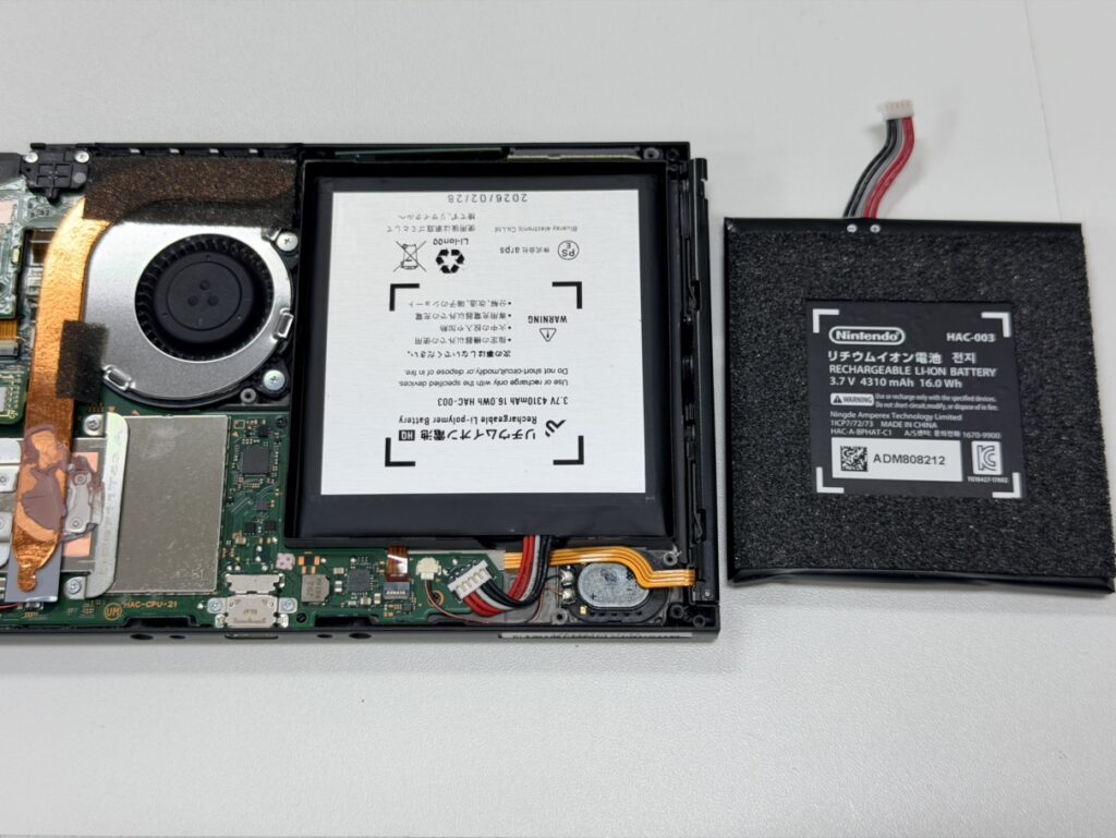 Switchの裏蓋を開け、冷却ファンのホコリを掃除しながらバッテリーを取り外す様子。