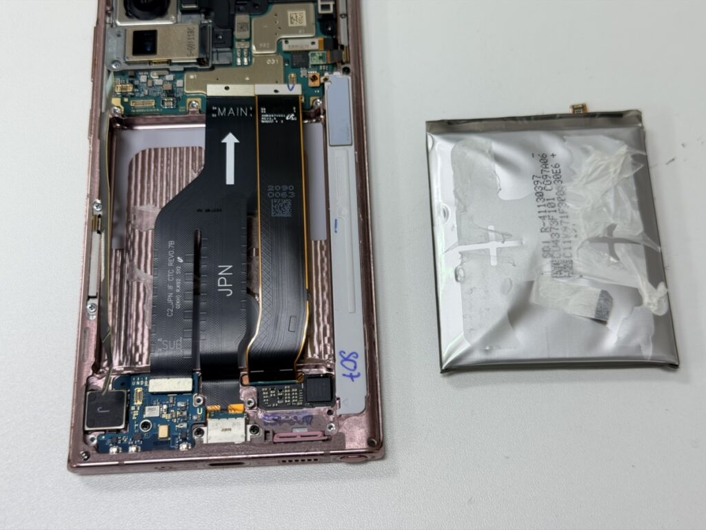 Galaxy Note20 Ultraの背面から、経年劣化でパンパンに膨らんだ古いバッテリーを安全に取り外す様子。